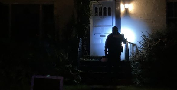 Police officer shines a flashlight on home
