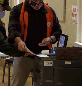 Poll workers feeding ballots into a machine