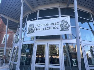 A plastic banner reads "Jackson-Reed High School" above glass doors.