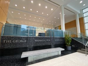 The lobby of George Washington University's student center is shown, with rows of pot lights illuminating a marble platform upon which a bench is placed.