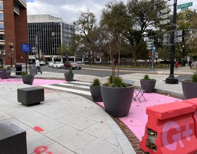 a converted U-turn lane south of Dupont Circle. there are planters and chairs between two pink barriers. the roadway is also painted pink.