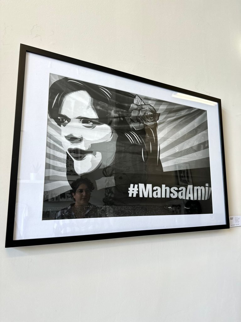 Mina Jafari's reflection is shown in a framed photo of Mahsa Amini displayed on a wall.