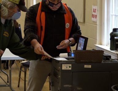 Poll workers feeding ballots into a machine