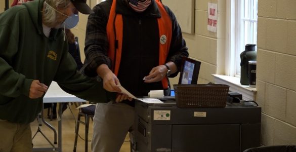 Poll workers feeding ballots into a machine