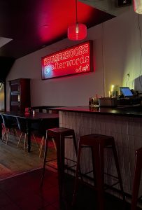 a photo of the end of a bar with a neon sign on the wall. the text of the neon says "Kramerbooks & Afterwords, a cafe"