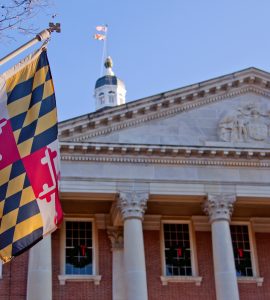 A close up view of the Maryland Statehouse with a state flag in the foreground The Maryland Statehouse with a state flag in the foreground. (Courtesy Glynnis Jones / Adobe Stock)