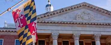 A close up view of the Maryland Statehouse with a state flag in the foreground The Maryland Statehouse with a state flag in the foreground. (Courtesy Glynnis Jones / Adobe Stock)
