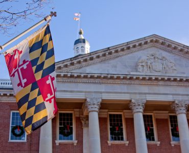A close up view of the Maryland Statehouse with a state flag in the foreground The Maryland Statehouse with a state flag in the foreground. (Courtesy Glynnis Jones / Adobe Stock)