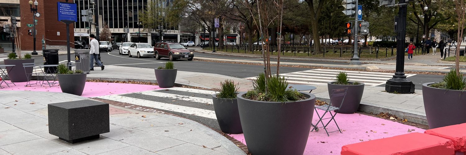 a converted U-turn lane south of Dupont Circle. there are planters and chairs between two pink barriers. the roadway is also painted pink.