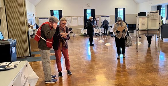 Election workers look at ballot together to help voter waiting nearby