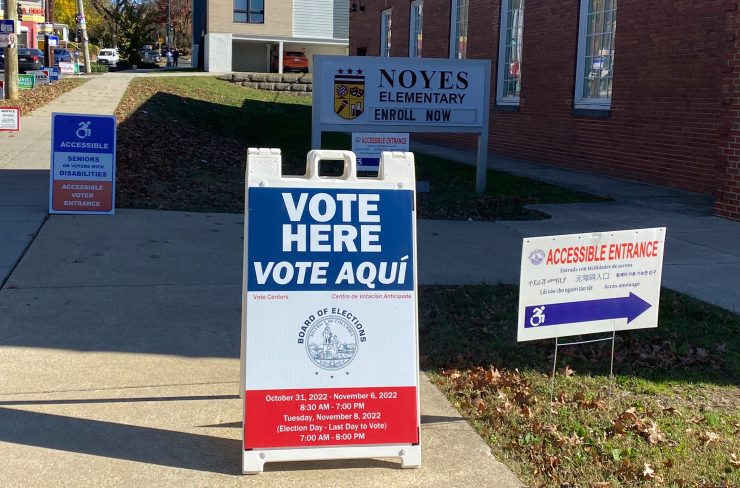 Voting signs in the foreground, placed in front of a school being used as a polling place.