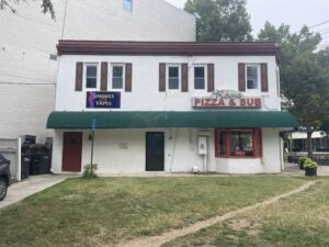 A white store with a sign for a pizza parlor and a smoke shop.