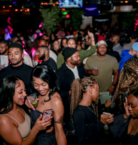 Amid the lively club scene, two friends share a moment of laughter as they look at a phone, capturing the modern nightlife trend of blending social media with in-person experiences. Photo taken by Andre R /Used with permission.