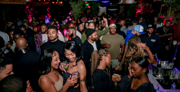 Amid the lively club scene, two friends share a moment of laughter as they look at a phone, capturing the modern nightlife trend of blending social media with in-person experiences. Photo taken by Andre R /Used with permission.