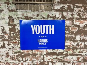 Blue "Youth for Harris-Walz" sign against a brick wall. 