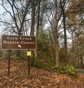 A sign for the Rock Creek Nature Center stands amid autumn leaves in Rock Creek Park. Photo by Jordan Thorton.