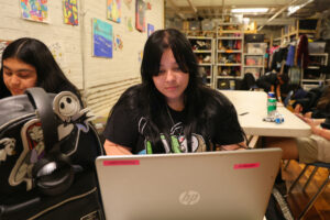 Balaria Rodríguez, next to friend Scarlet Serrano Santos, works on a graphic design flyer for Dia de Muertos on her laptop (Kelly Doyle)
