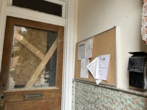 The front stoop of the property on the corner of Fuller Street and Mozart Place. The door is boarded up, and Samaritan Inn documentation from D.C. agencies still hangs on the bulletin board. (Isabel Del Mastro)
