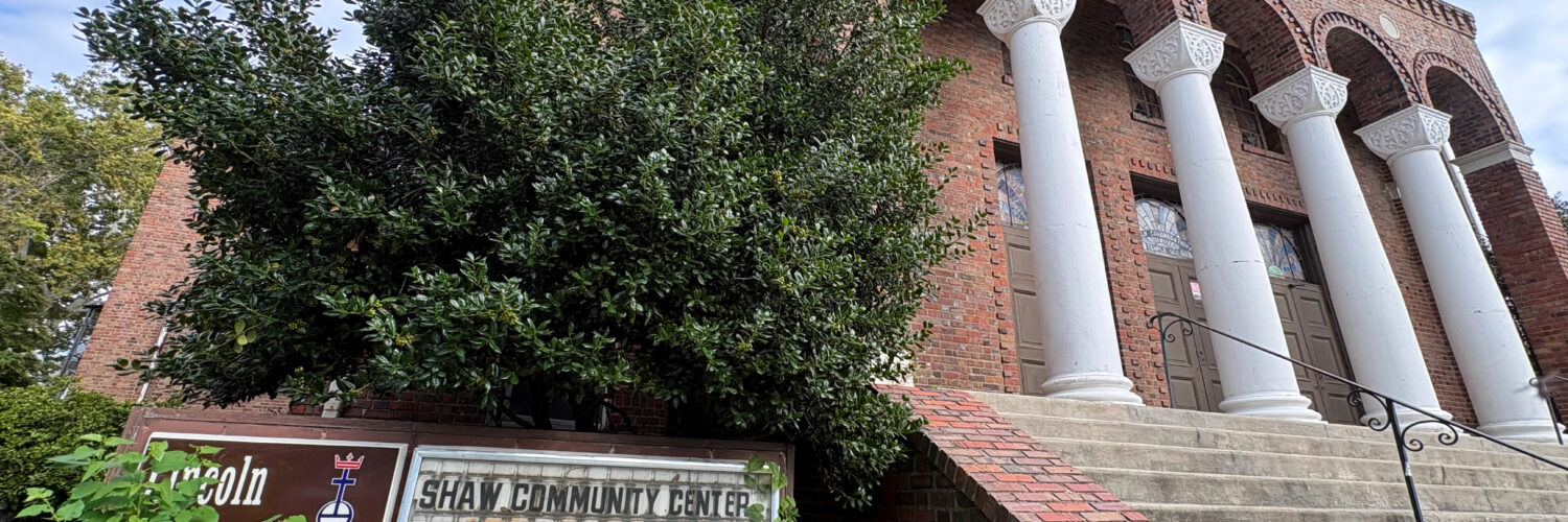 Looking up at the historic Lincoln Temple, an overgrown sign reads "Lincoln Congregational Temple United Church of Christ" and "Shaw Community Center 1701 11 St NW is open."