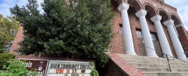 Looking up at the historic Lincoln Temple, an overgrown sign reads "Lincoln Congregational Temple United Church of Christ" and "Shaw Community Center 1701 11 St NW is open."