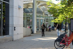 A person rides an electric scooter along the sidewalk outside the NoMa-Gallaudet U Metro station entrance.