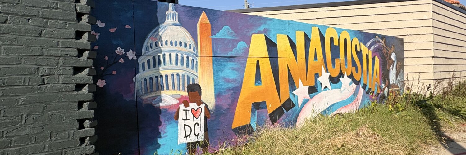 At a central entrance to the historic Anacostia neighborhood, a vibrant mural features the U.S. Capitol, the Washington Monument, and a brown-skinned person holding a poster that reads "I (heart) DC" on its left side. On the mural's right, a guitarist, trumpet player, and pianist play their respective instruments. Between the scenes, "Anacostia" arcs along a whimsical renderings of the lines and stars in D.C.'s flag.