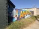 At a central entrance to the historic Anacostia neighborhood, a vibrant mural features the U.S. Capitol, the Washington Monument, and a brown-skinned person holding a poster that reads "I (heart) DC" on its left side. On the mural's right, a guitarist, trumpet player, and pianist play their respective instruments. Between the scenes, "Anacostia" arcs along a whimsical renderings of the lines and stars in D.C.'s flag.