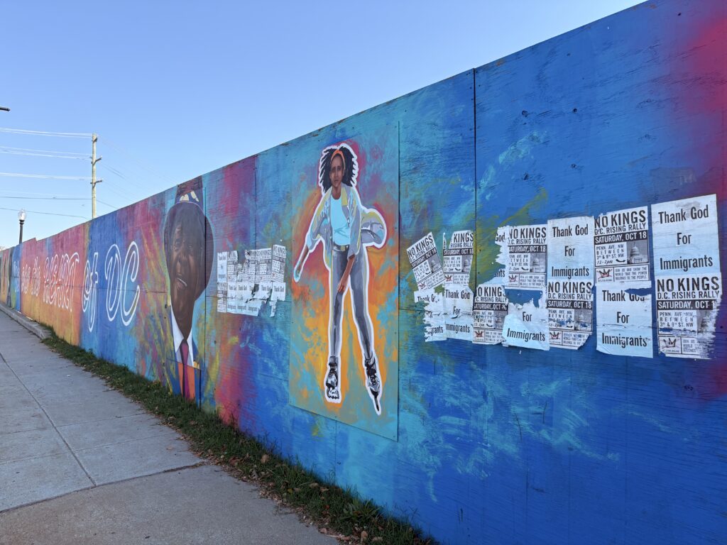 Cerulean, teal, tangerine, fuschia, and violet hues stretch across the barriers of a bridge. A deep brown-skinned senior, wearing a hat, suit, and tie, smiles. Flanked by black and white "NO KINGS" rally and "Thank God for Immigrants" posters, a brown-skinned woman ice skates forward. The mural has painted white, cursive lettering that reads, "We are the HEART of DC." 