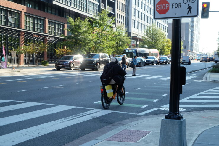 A cyclist rides into a Florida Avenue intersection as pedestrians cross in front of him and a traffic signal displays red.